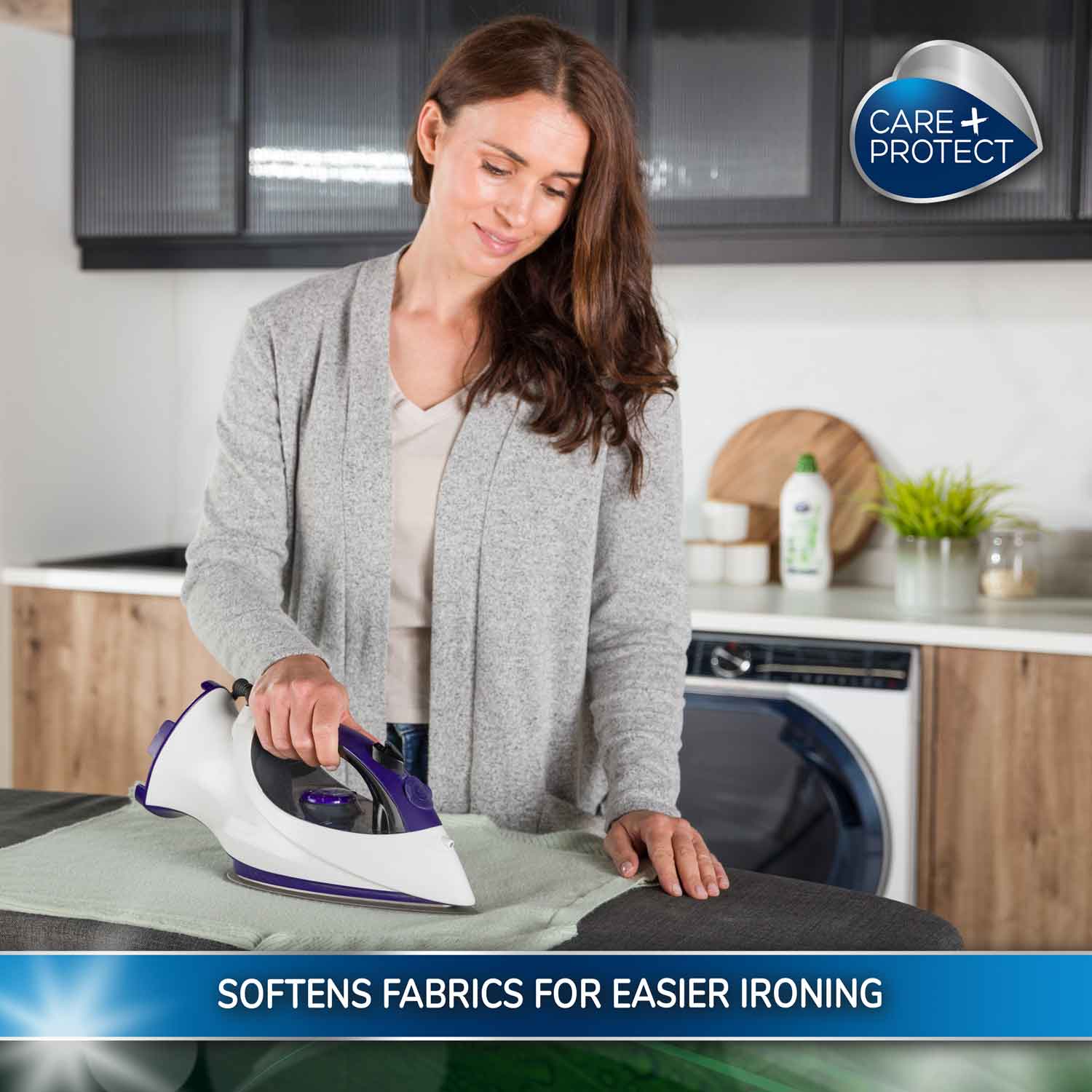 Woman uses an iron to press a green cloth in a modern kitchen with wooden cabinets. A "Care+Protect" logo is above. Text reads: "SOFTENS FABRICS FOR EASIER IRONING."