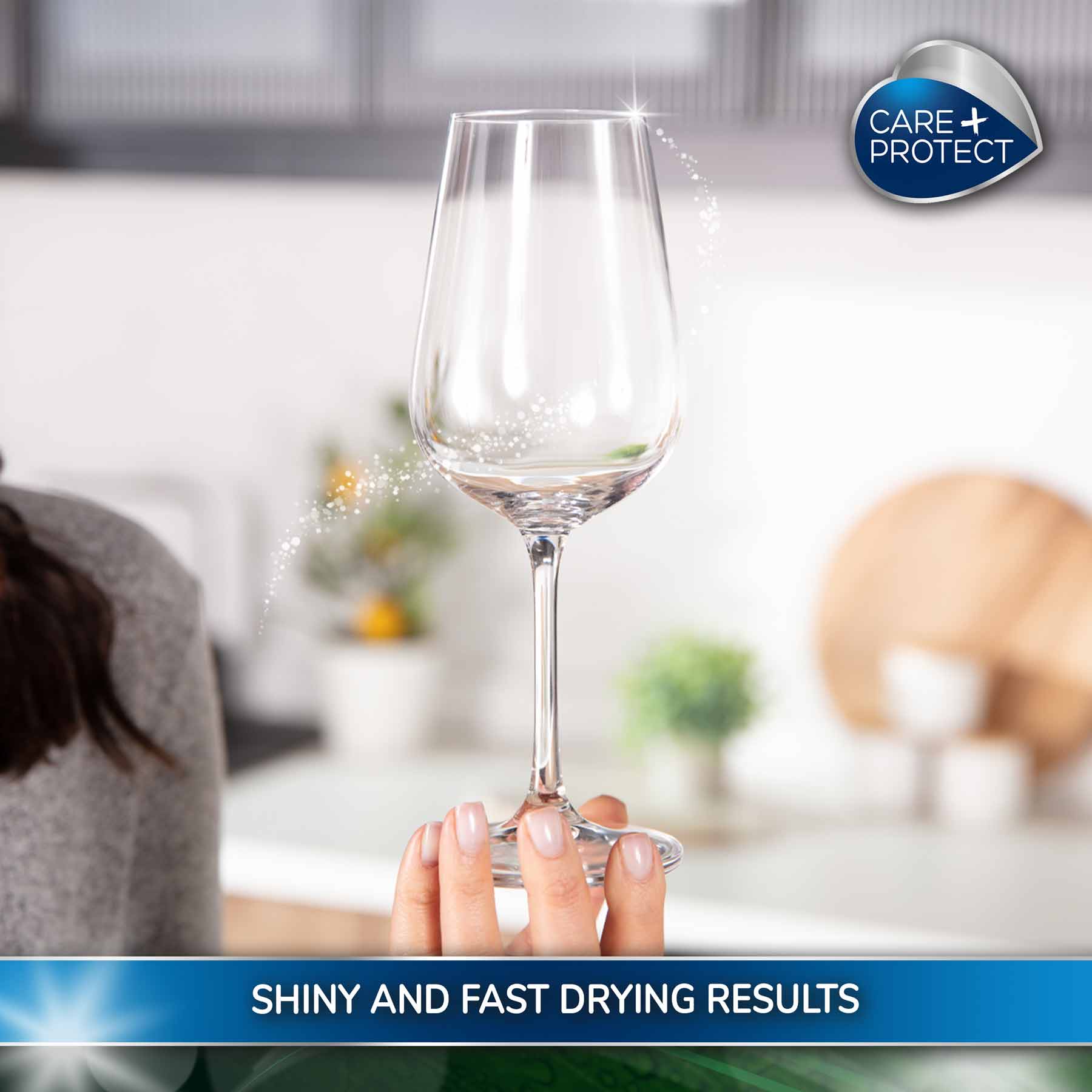 A hand holds a sparkling wine glass aloft in a bright kitchen. Text: "SHINY AND FAST DRYING RESULTS." A "CARE + PROTECT" label is in the top right corner.