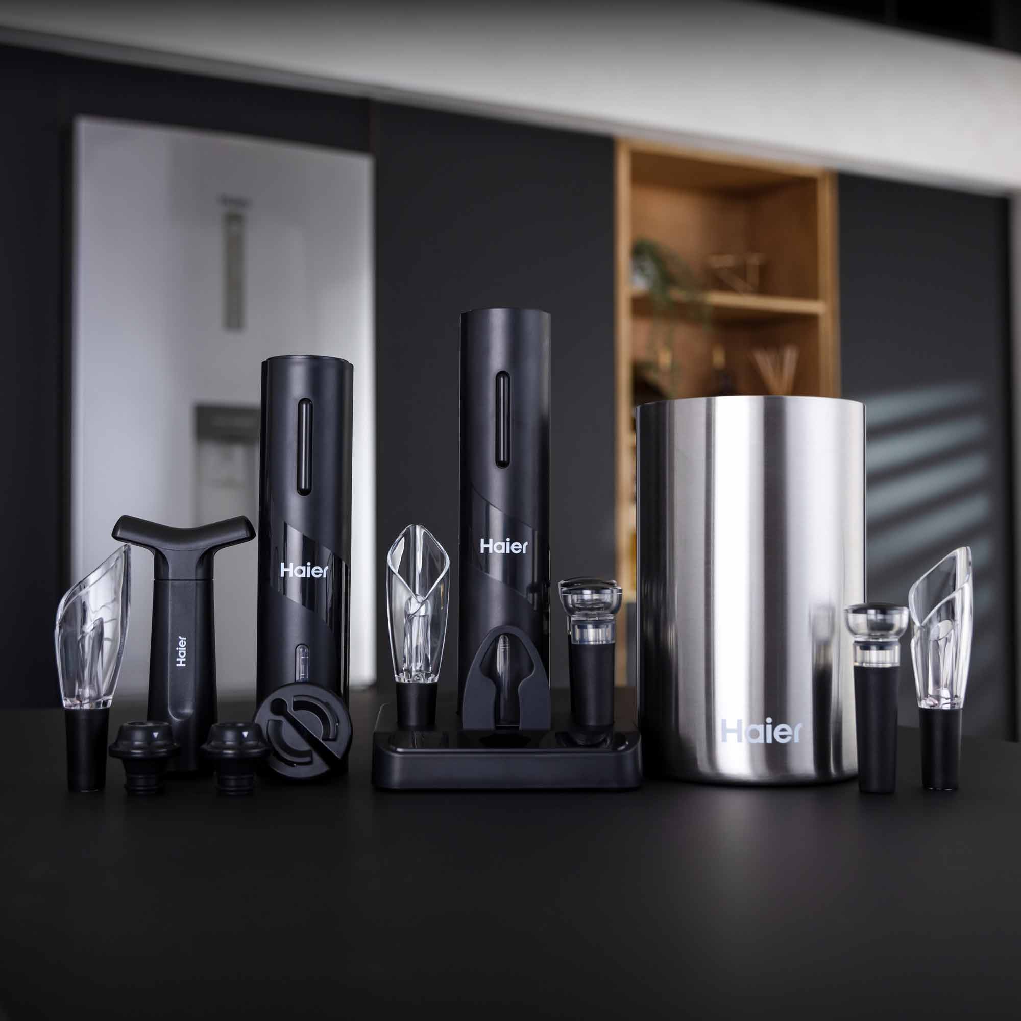 A collection of Haier wine accessories, including electric openers, aerators, and a sleek stainless steel cooler, arranged on a black surface within a modern room setting.