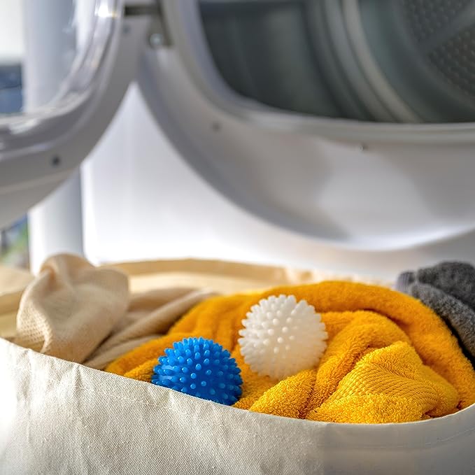 Spiky blue and white dryer balls rest on bright yellow towels inside an open clothes dryer, enhancing the laundry's softness in a utility room environment.