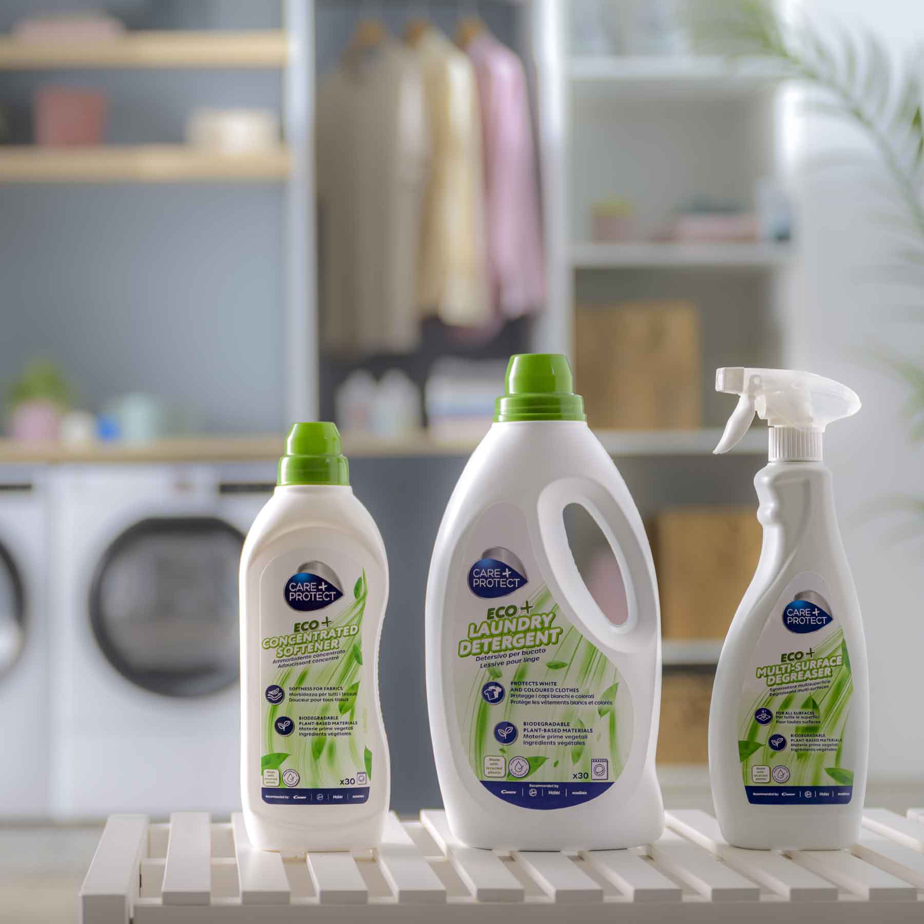 Three laundry care products with green lids are on a white shelf: "Eco concentrated softener," "Eco laundry detergent," and "Eco multi-surface degreaser." A laundry room setting is visible behind.